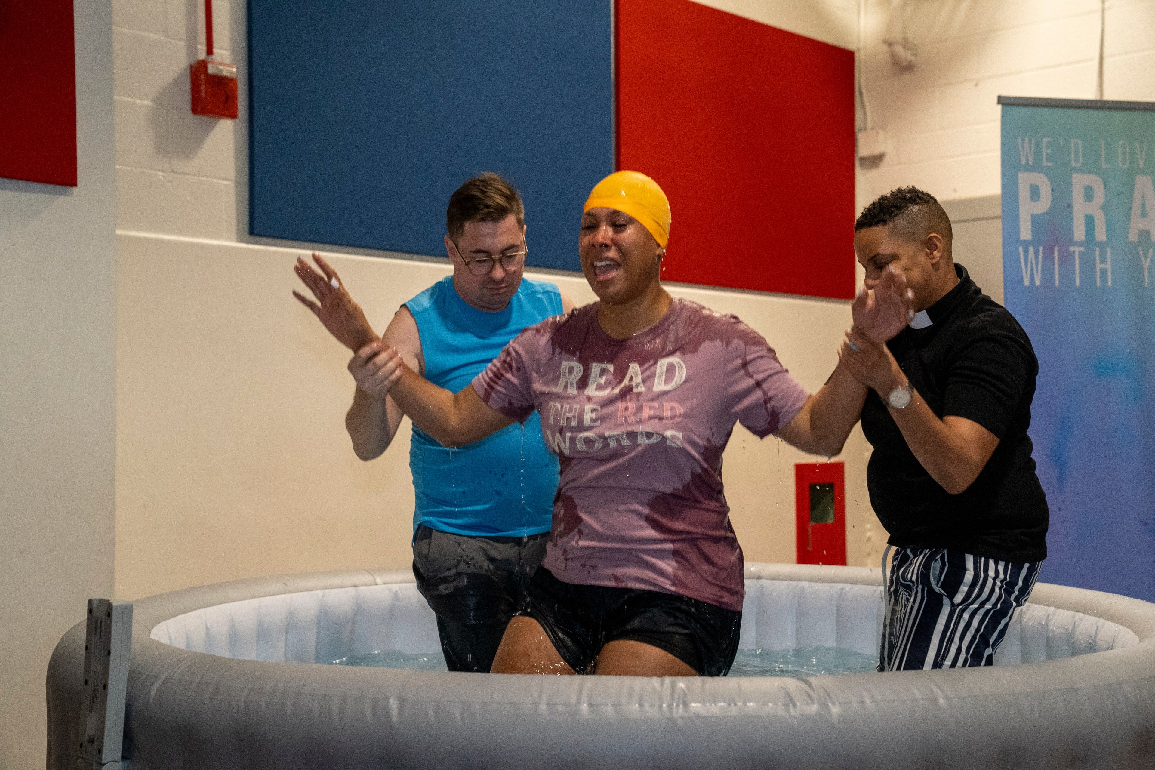 A woman is baptized, arms raised, in an inflatable pool as two people help her up.