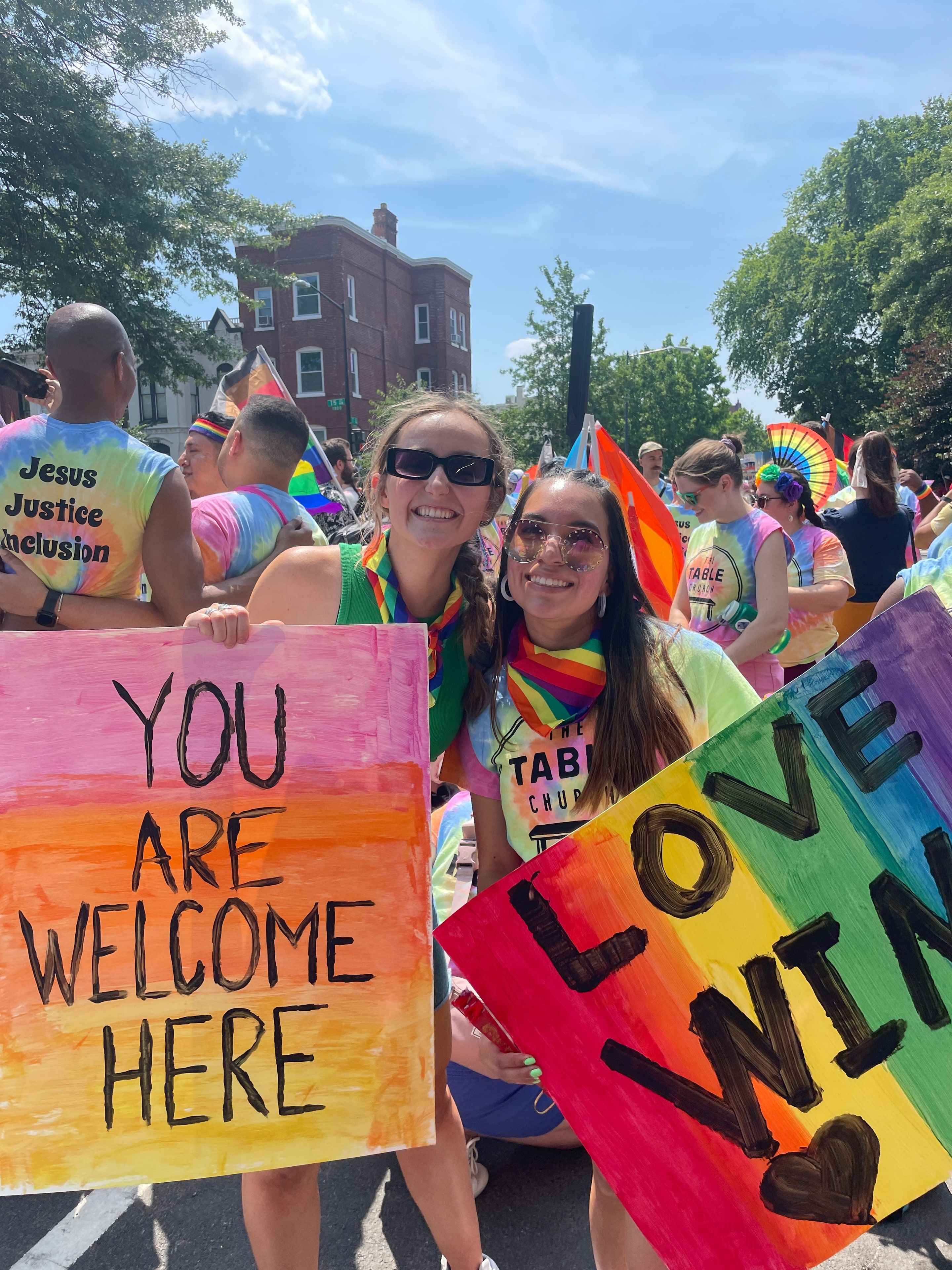 Two people at Capital Pride hold signs reading 'You are welcome here' and 'Love wins.'