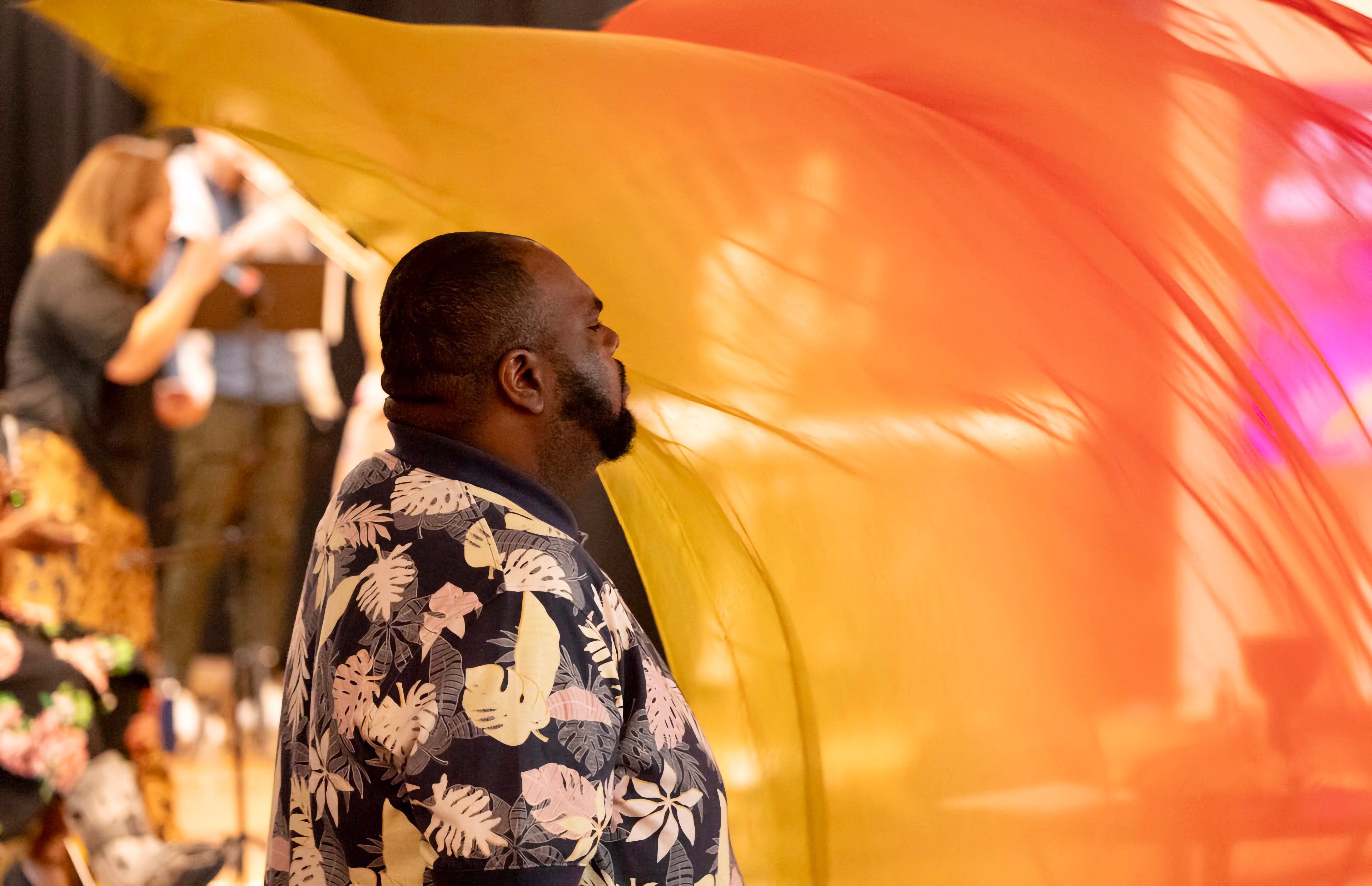 A worshiper stands under a sweep of orange and gold fabric during a Sunday service at The Table.