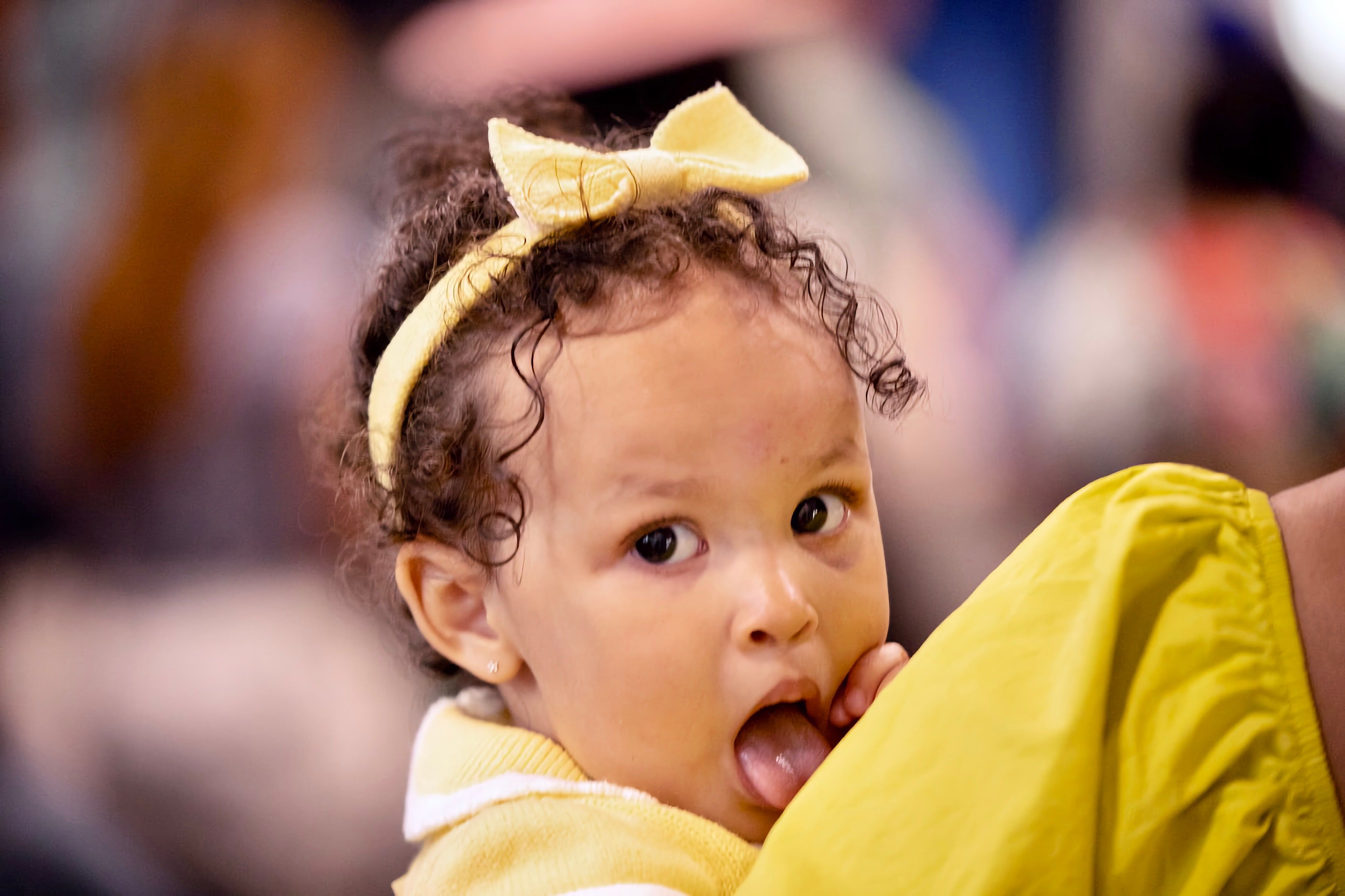 A toddler with a yellow bow looks over a parent's shoulder during worship.