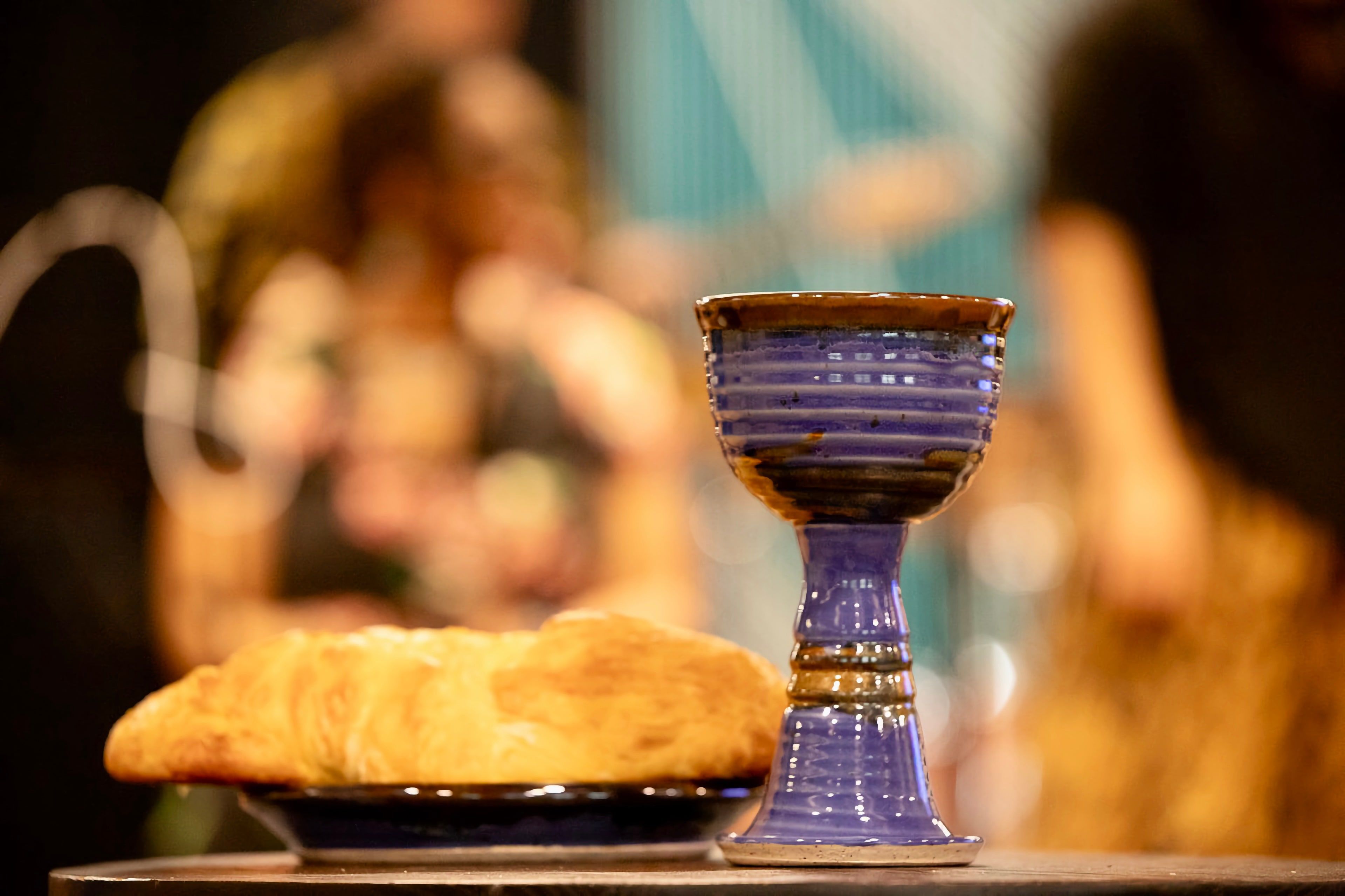 A pottery chalice and a round loaf of bread on the Communion table, with the band blurred behind.