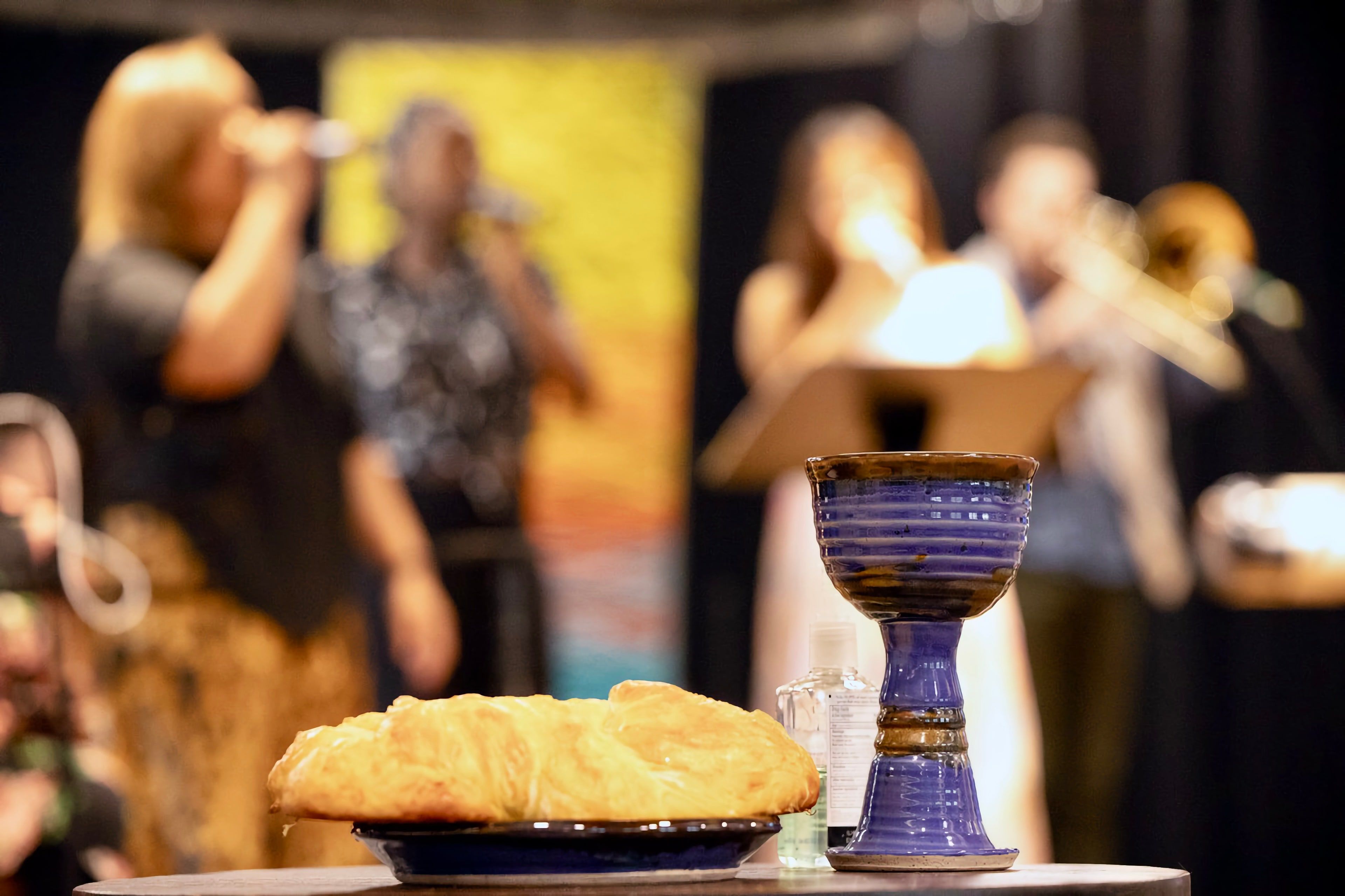 A loaf of bread and a pottery chalice on the Communion table, with the band behind.